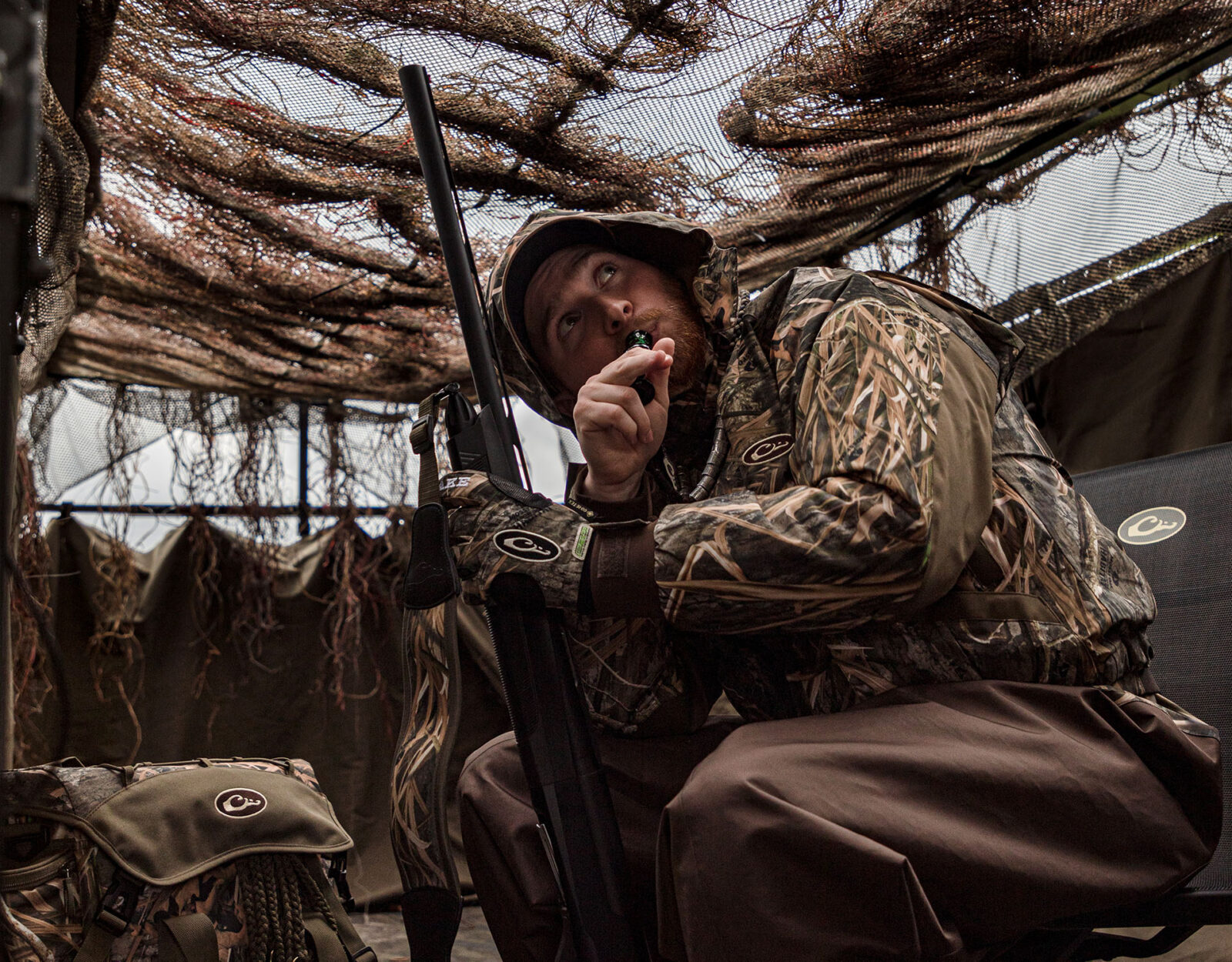 A duck hunter in full camo hiding in a duck blind 