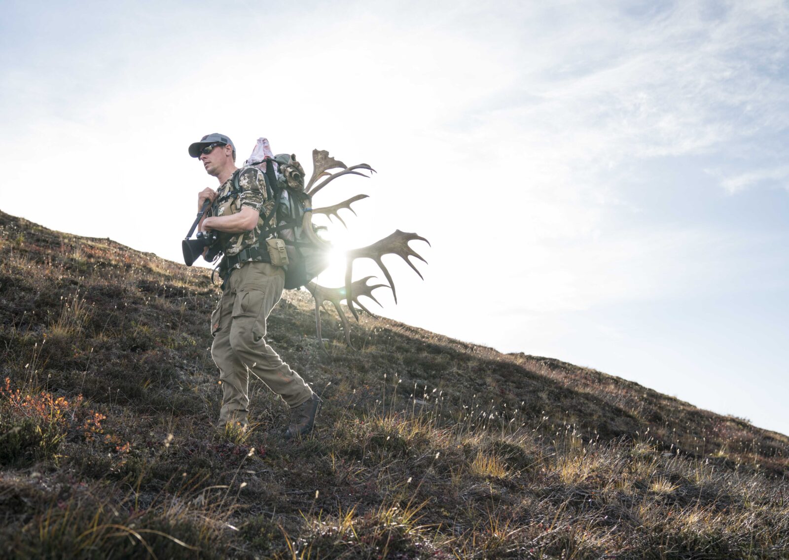 A hunter walking ver a ridge with antlers on his back