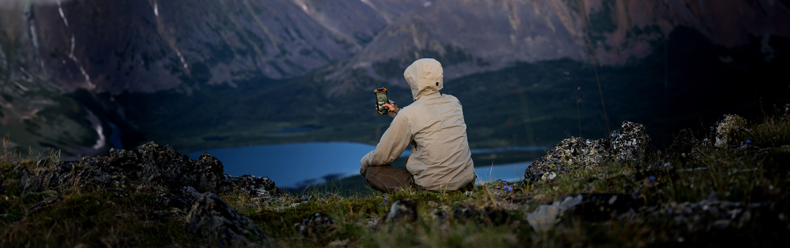 Someone looking over a mountain ridge into a lake while using the onX Hunt app on their phone