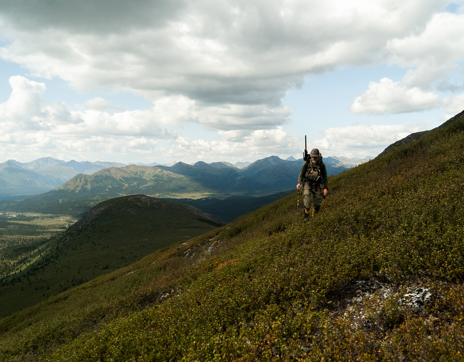 A rifle hunter walking a ridge with mountains in the background 