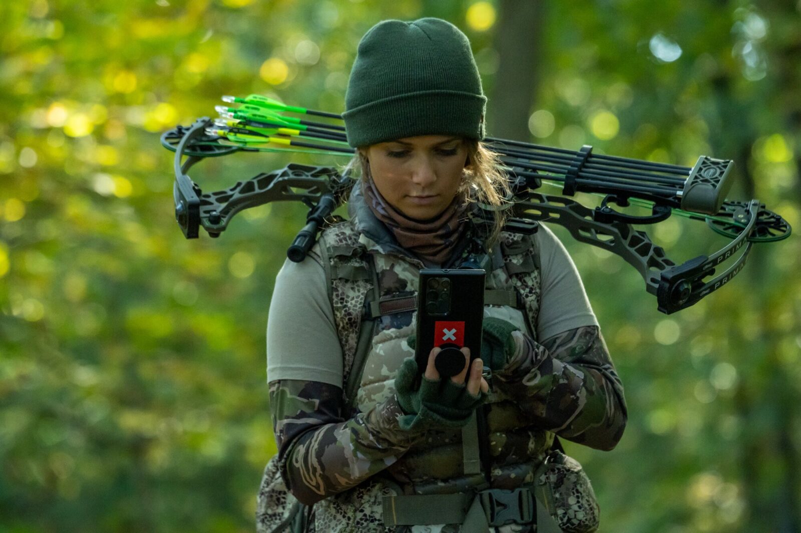 A female hunter in all camo with a crossbow on her back using the onX Hunt app.