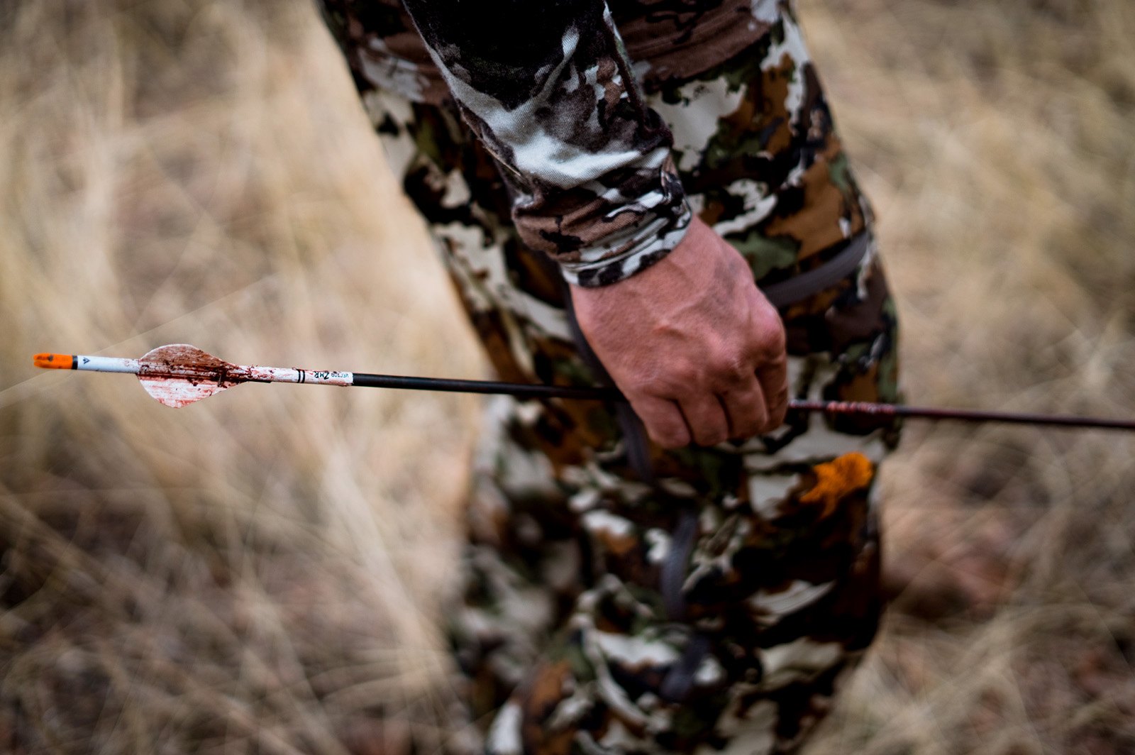 A close up of a male's hand holding a bloodied arrow. 