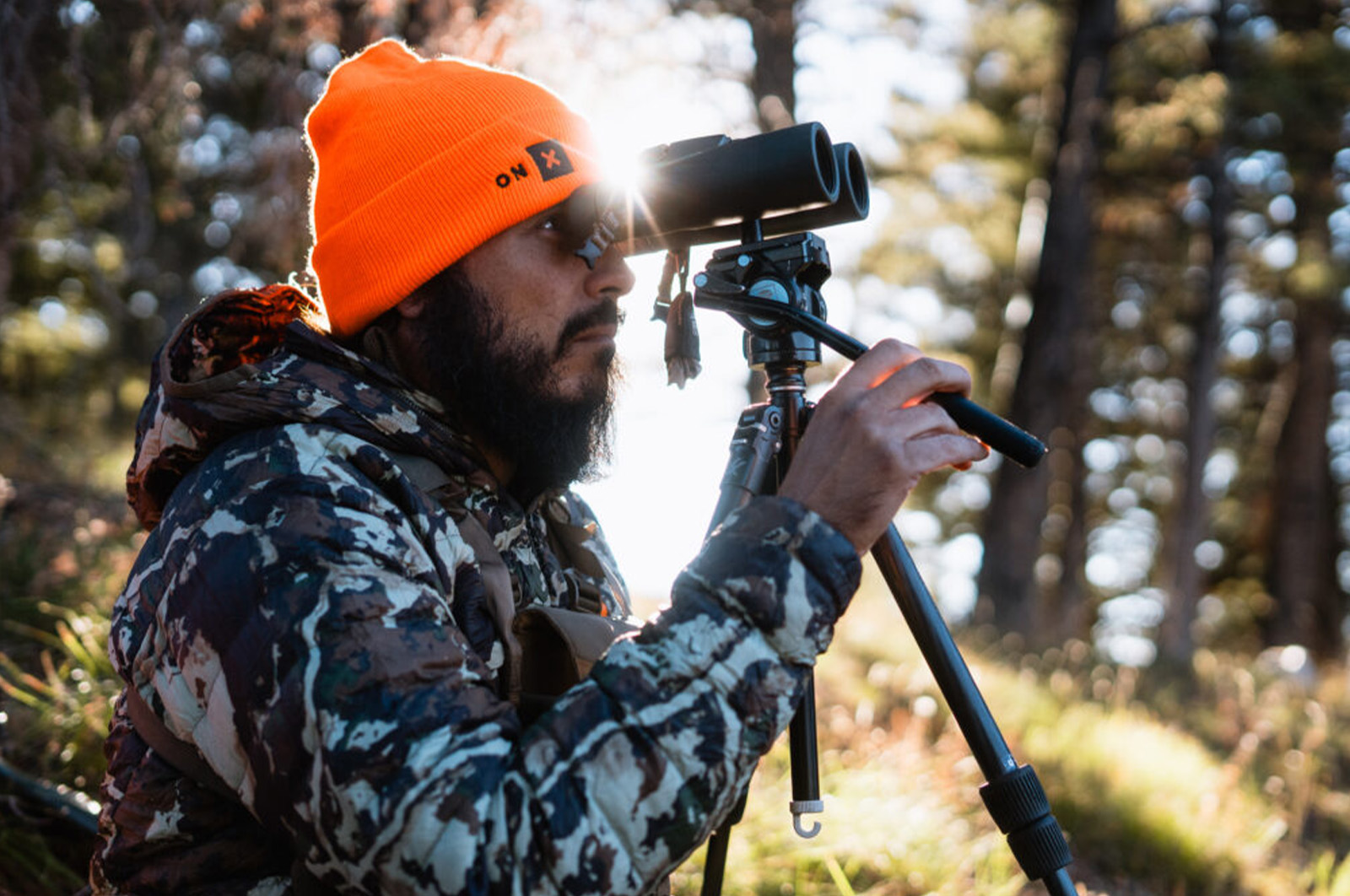 Man in camouflage and blaze orange hat glassing in mountains.