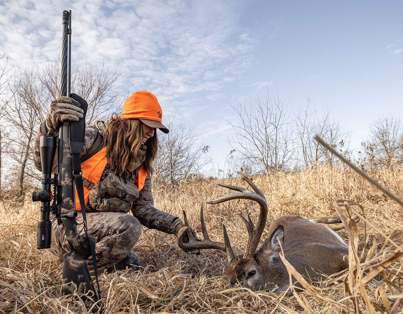 A female hunter admires a downed whitetail buck. 