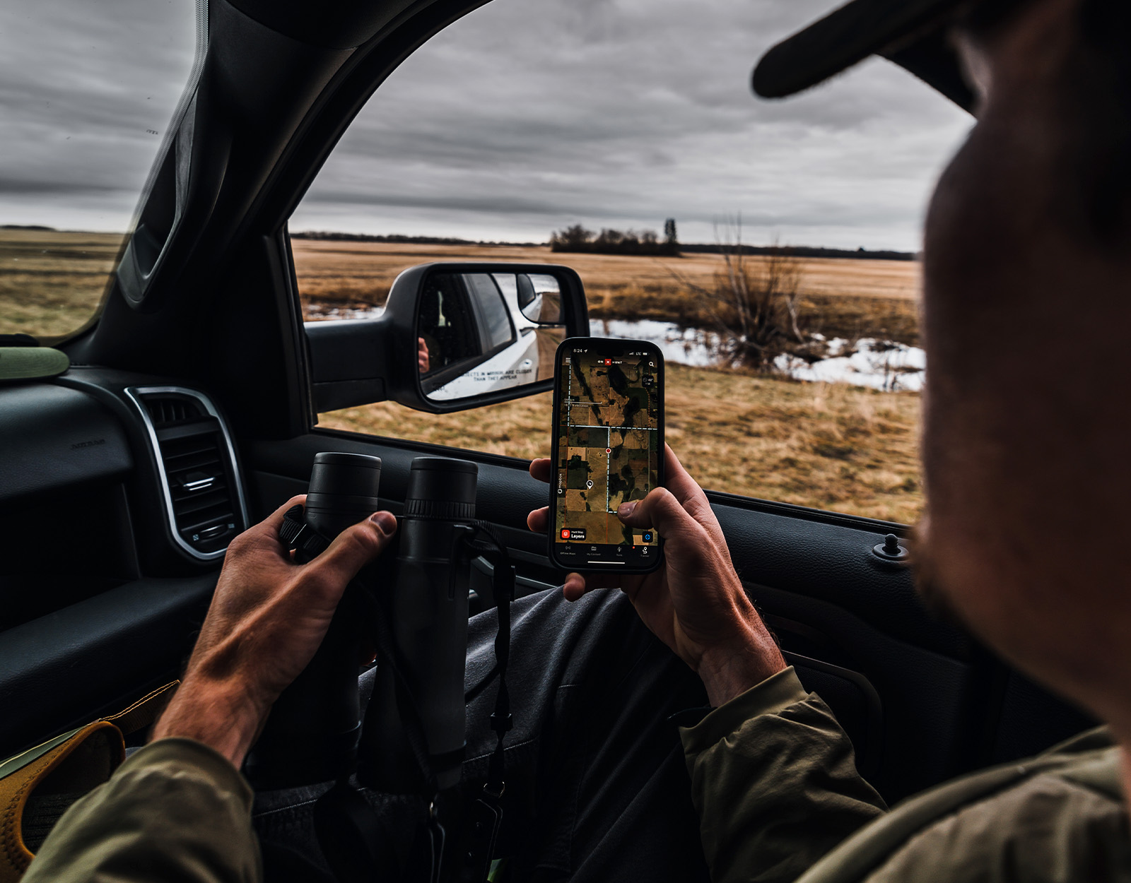 A hunter references onX Hunt while in a vehicle holding binoculars.